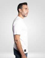 Vista de perfil de modelo con camiseta blanca faaia, mostrando el ajuste y un tatuaje en el brazo
