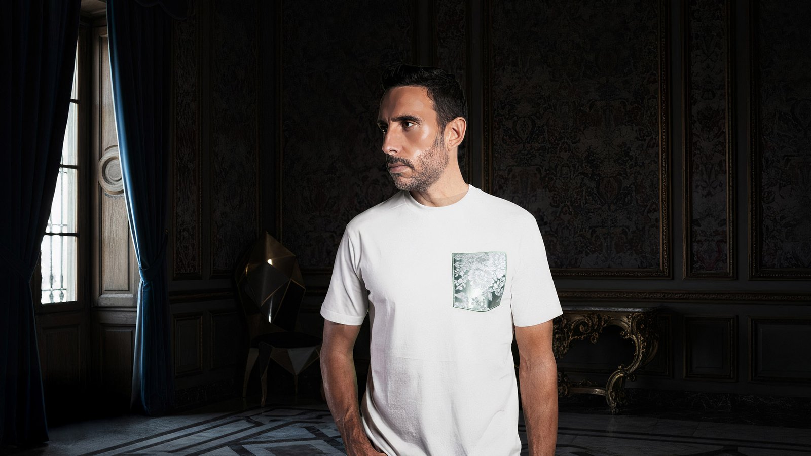 Modelo con camiseta blanca faaia posando de perfil en un interior clásico y elegante con paredes oscuras