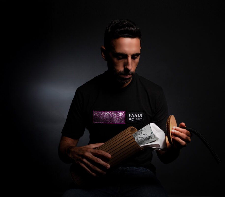 Modelo masculino vistiendo una camiseta negra de algodón marca faaia, con un detalle rectangular de tela fallera fucsia y plata en el pecho, abriendo el packaging creativo de la marca..