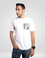 Hombre posando con la camiseta blanca faaia que lleva un bolsillo de tela fallera en tonos verdes y azules