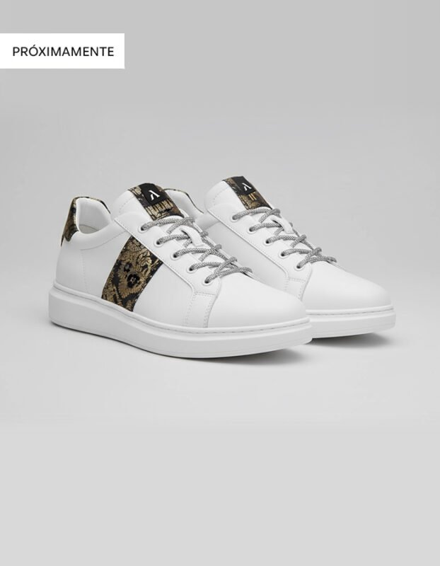 Par de zapatillas blancas de piel para hombre con cordones blancos y una banda lateral confeccionada con tela fallera de diseño ornamental