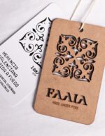 Etiqueta de madera sostenible cortada a fuego y etiqueta de cartón blanco reciclado de la marca Faaia Moda con tela fallera.