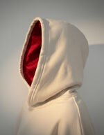 Primer plano de la sudadera Faaia en blanco roto con capucha forrada en damasco de seda rojo.