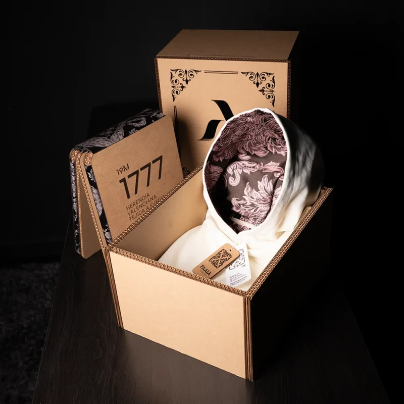 Sudadera blanca Faaia con capucha con tela fallera marrón y rosa insertada en un estuche experiencial.