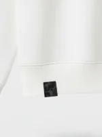 Detalle etiqueta de fragmento de tela fallera en faldón de sudadera blanca marca Faaia.