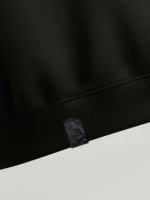 Detalle de etiqueta de tela fallera damasco negro aplicado en el bajo de una sudadera.