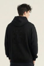 Joven modelo de espaldas con sudadera Faaia que tiene un bordado ornamental en la parte trasera y tela damasco negra en la capucha.