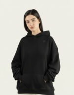 Mujer joven con sudadera negra oversize marca Faaia que incorpora tela damasco negra en la capucha.