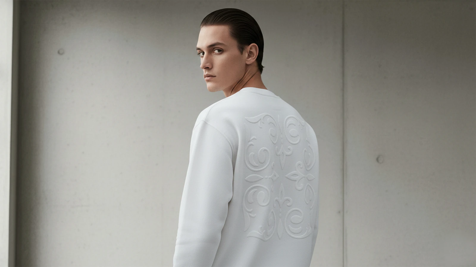 Modelo hombre joven posando de espaldas con una sudadera de la marca Faaia que lleva un bordado ornamental blanco al tono.