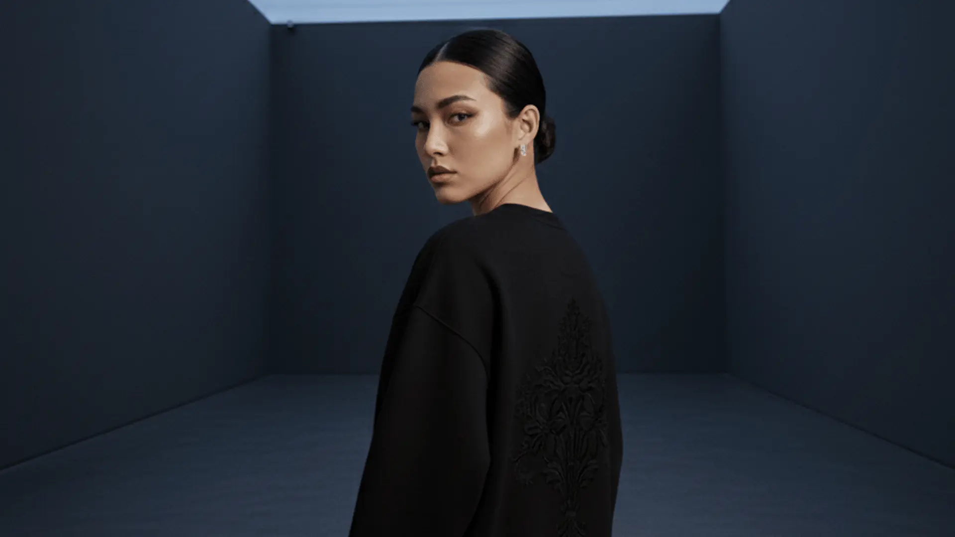 Mujer joven con el pelo oscuro posa con una sudadera negra con un bordado espectacular d la marca Faaia