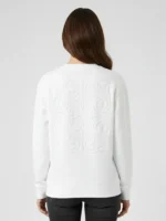 Mujer joven posando de espaldas con una sudadera de color blanco y bordado ornamental al tono en la espalda marca Faaia moda.