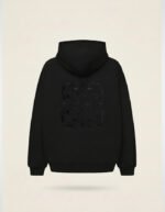 Vista frontal de sudadera oversize Faaia negra con tela damasco tejida en la capucha.