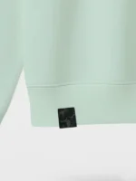 Etiqueta de tela damasco negra aplicada en sudadera de color verde agua marca Faaia.