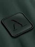 Icono marca Faaia con relieve aplicado en etiqueta de micro inyección negra sobre fondo verde botella.