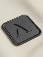 Icono marca Faaia con relieve aplicado en etiqueta de micro inyección negra sobre fondo blanco tierra.