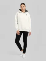 mujer joven posando de frente a la camara con una sudadera blanca con la capucha forrada en brocatel Santa Ana azul de la marca Faaia.