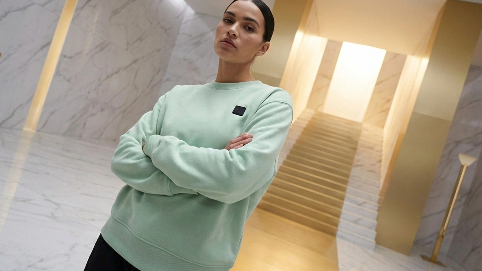 Mujer joven con pelo oscuro posando con una sudadera verde agua de la marca Faaia hecha en Valencia.