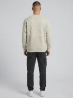 Hombre joven posando de espaldas a la cámara con una sudadera de color tierra que tiene un bordado ornamental al tono de la marca Faaia.