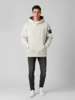 Hombre joven posando con sudadera gris claro marca Faaia con brocatel color burdeos en el interior de la capucha.