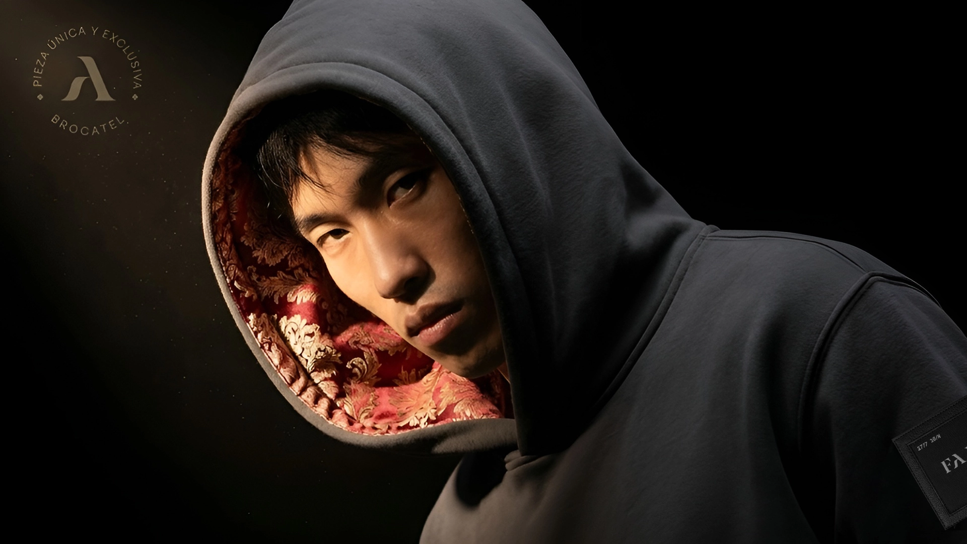 Hombre joven posando con una sudadera gris ebony de la marca Faaia con capucha en brocatel ornamental sofisticado.