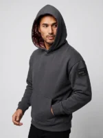 Hombre joven posando con sudadera gris ebony con brocatel sofisticado en la capucha y bordado ultra premum en la espalda al tono.