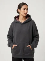 Mujer joven posando con una sudadera de la marca Faaia de color gris ebony con brocatel ornamental en la capucha.