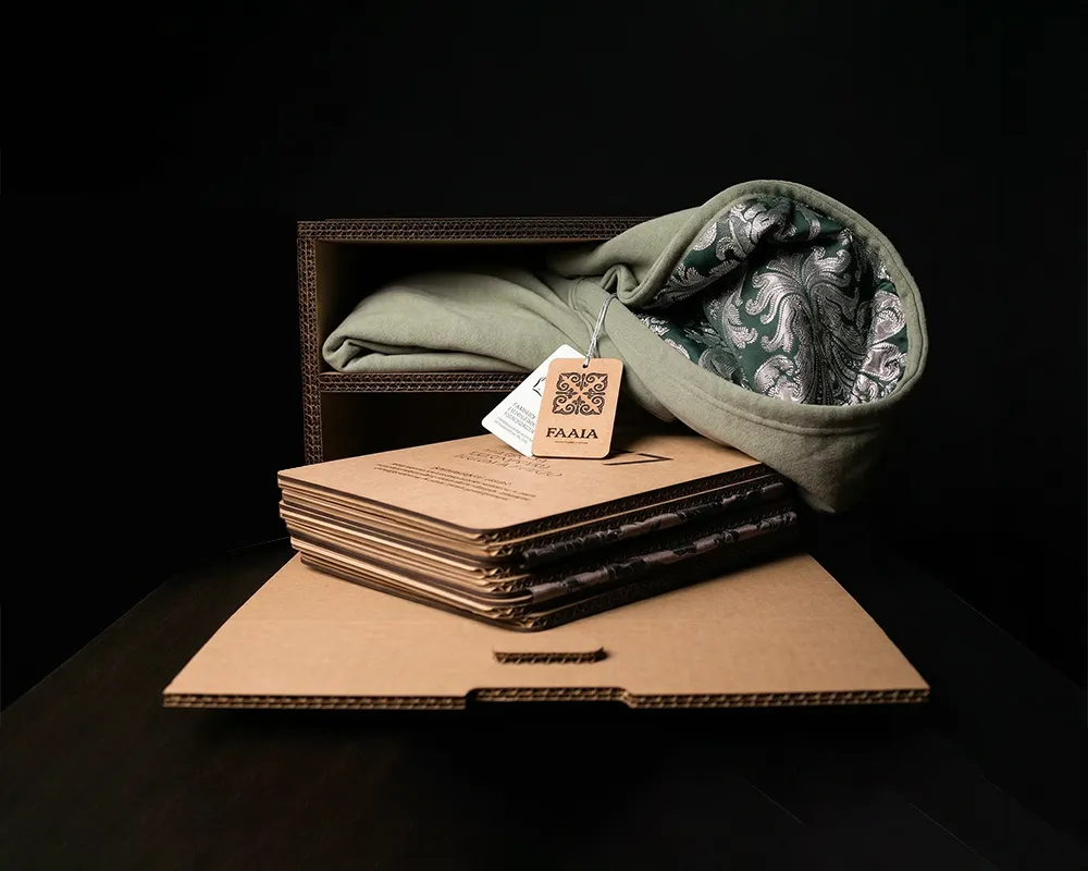 Sudadera con un damasco verde y plata forrado en la capucha dentro de una caja de cartón a modo de estuche experiencial de Faaia moda valenciana.
