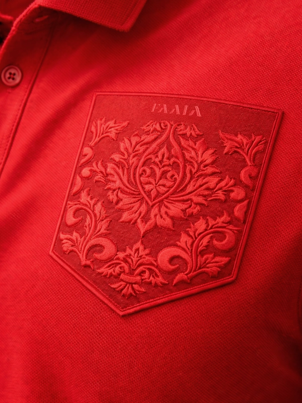 Plano principal de falso bolsillo bordado con damasco valenciano y logo Faaia en polo piqué de color rojo.
