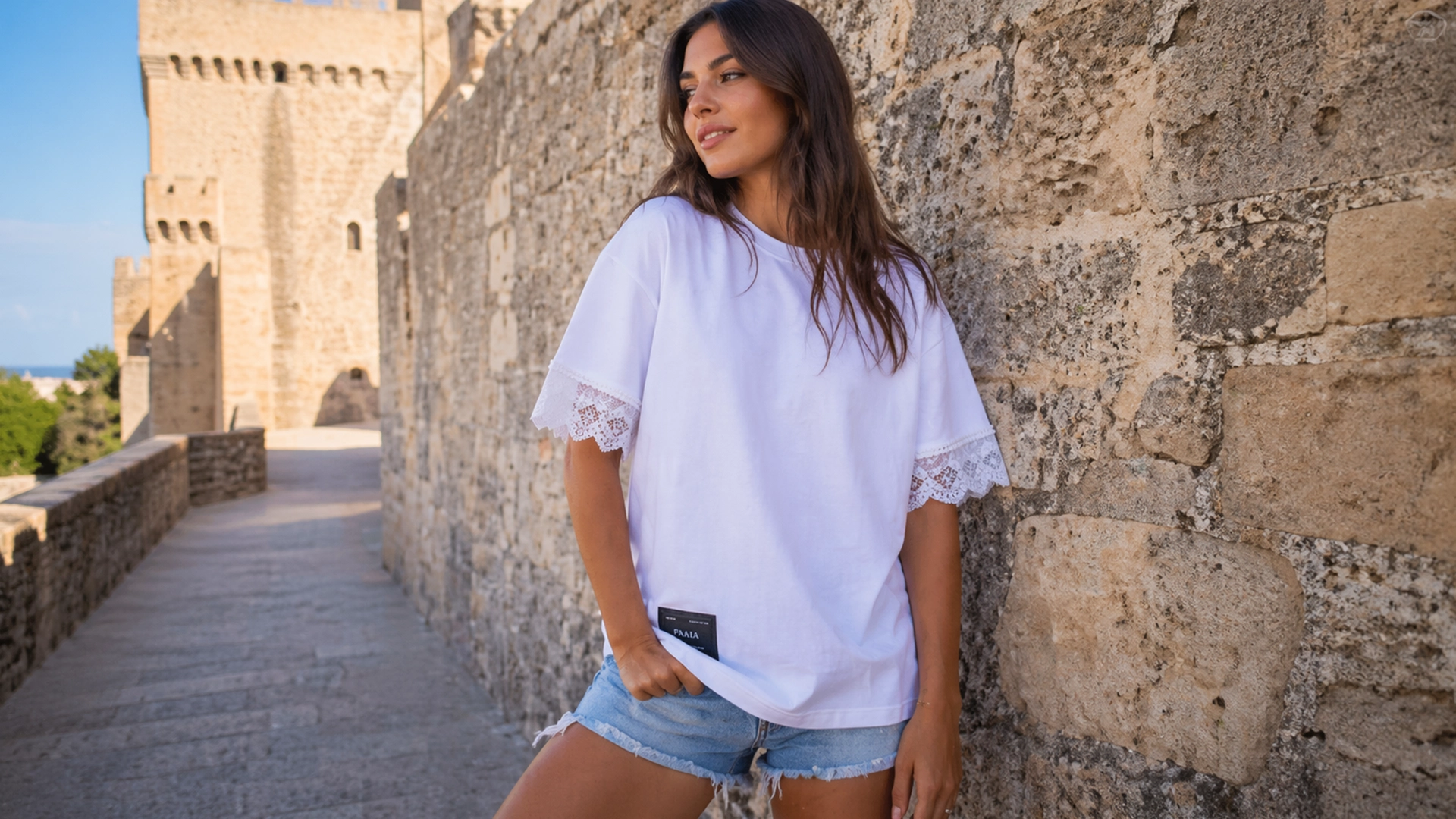 Mujer joven posando con una camiseta de la marca Faaia de color blanco con corte oversize con un detalle de puntilla insertado en las mangas.