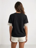 Mujer joven de espaldas posando con una camiseta sofisticada de color negro de la marca Faaia que integra puntilla blanca en las mangas.