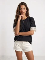 Mujer joven posando con una camiseta negra de la marca Faaia hecha para mujeres que buscan detalles como la puntilla que integra en las mangas.