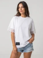 Mujer joven posando con camiseta de manga corta de colr blanco y corte oversize de la marca Faaia que integra puntilla como detalle exclusivo.