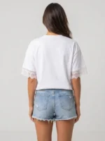 Mujer joven posando de espaldas con una camiseta de la marca Faaia que integra puntilla en las mangas.