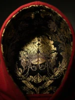 Primer plano del interior de una capucha de sudadera de color roja forrada con un brocatel de color negro y dorado marca Faaia.