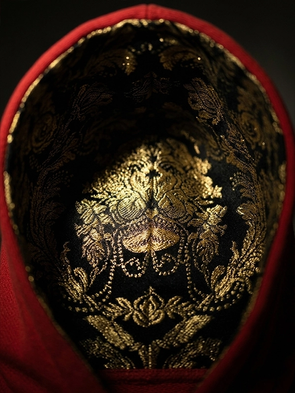 Primer plano del interior de una capucha de sudadera de color roja forrada con un brocatel de color negro y dorado marca Faaia.