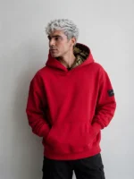 Hombre modelo joven posando con una sudadera de color rojo vivo con un forro de brocatel color negro y con hilo dorado en la capucha.