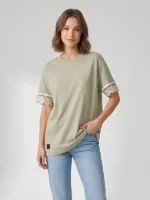 Mujer joven posando con camiseta oversize color tierra de la marca Faaia con puntilla valenciana en las mangas.