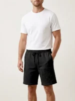 Hombre joven posando con pantalon corto marca Faaia de color negro con bordado ornamental tono sobre tono.