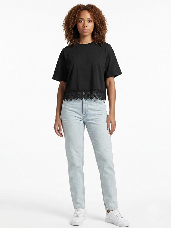 Mujer joven modelo posando con una camiseta negra con corte crop de la marca Faaiia que además fusiona puntilla valenciana.