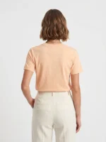 Mujer joven modelo posando de espaldas con una camiseta color melocotón.