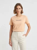 Mujer joven posando con camiseta regular color melocotón con el logo de Faaia en el pecho.