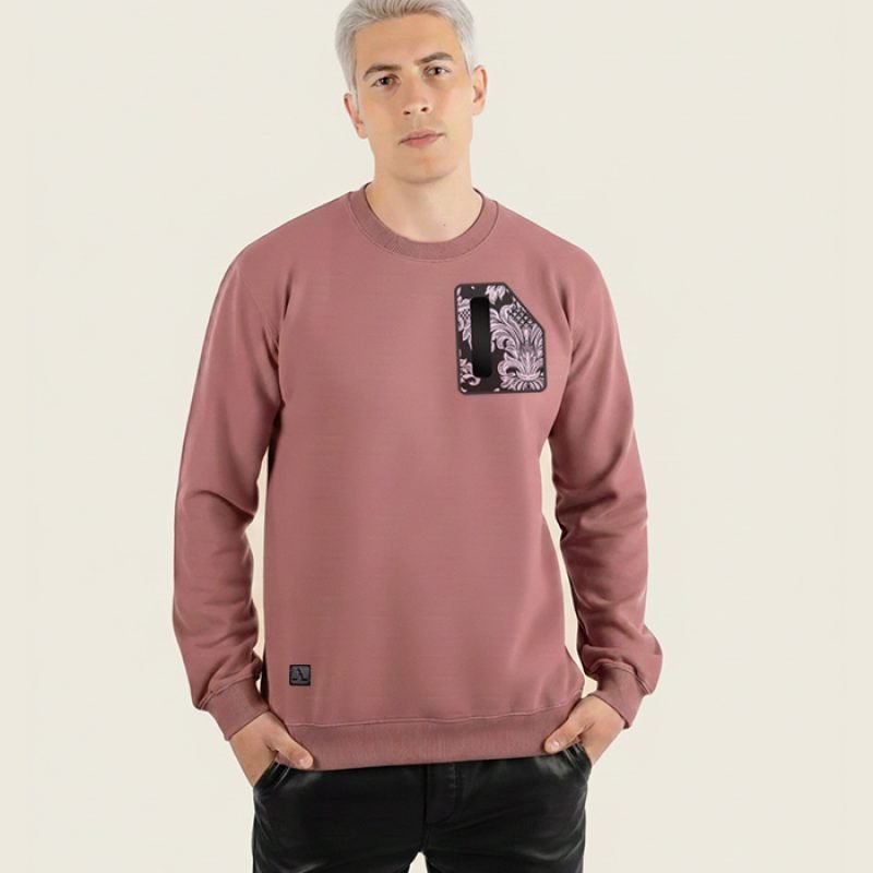 Hombre joven con sudadera de color burdeos de la marca Faaia que lleva un fragmento de damasco como el de las telas falleras en el pecho.